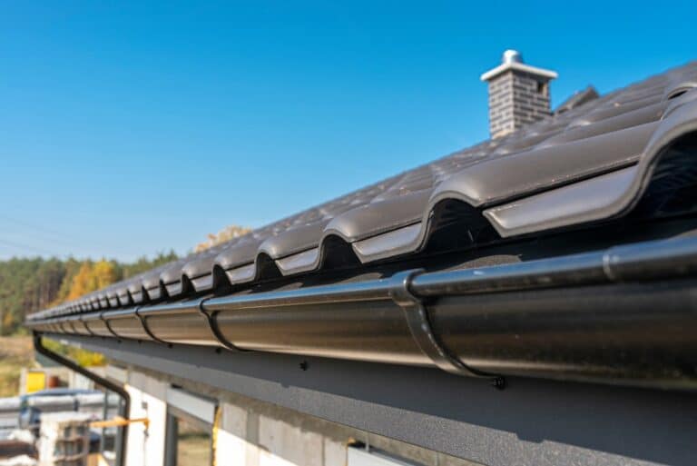 A metal, black gutter on a roof covered with ceramic tiles. Close up shot.